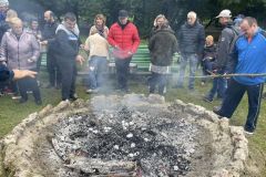 Ludzie stoją przy ognisku pieką ziemniaki