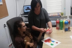 Uczestniczka z pomocą terapeuty maluje dłońmi lampion