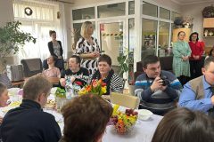 Uczestnicy podczas Spotkania Wielkanocnego siedzą przy stole, Dyrektor ŚDS składa najserdeczniejsze życzenia Wielkanocne