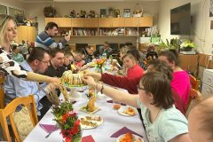 Uczestnicy podczas Spotkania Wielkanocnego siedzą przy stole, Dyrektor ŚDS częstuje babką