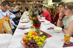 Uczestnicy podczas Spotkania Wielkanocnego siedzą przy stole, Dyrektor ŚDS składa najserdeczniejsze życzenia Wielkanocne