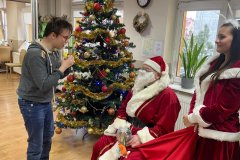 Uczestnik przy choince z Mikołajem i Śnieżynką dostaje prezent