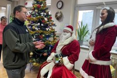 Uczestnik przy choince z Mikołajem i Śnieżynką dostaje prezent